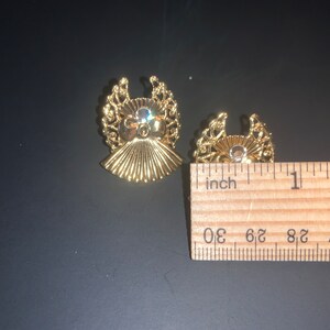 May include: Two gold-tone angel-shaped earrings with clear rhinestones in the center. The earrings are about 1 inch in diameter.