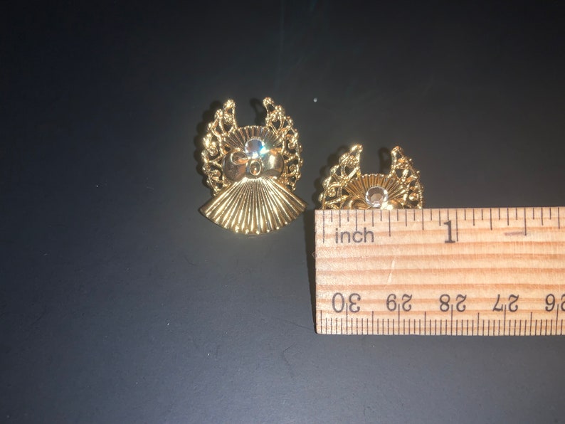 May include: Two gold-tone angel-shaped earrings with clear rhinestones in the center. The earrings are about 1 inch in diameter.