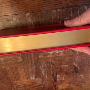 May include: The spine of a red hardback book with a gold-coloured band around the edge.