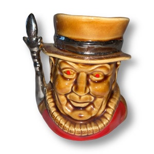 May include: A ceramic figurine of a man wearing a brown top hat and a red jacket. He has a brown beard and mustache and is holding a silver walking stick.