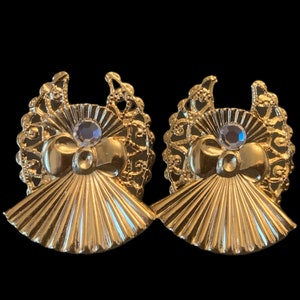 May include: A pair of gold tone earrings with a fan-shaped design and a clear rhinestone in the center of each earring.