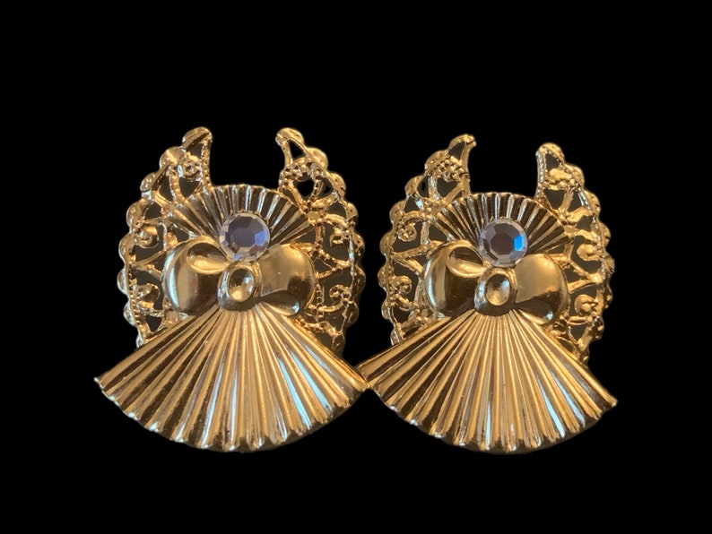 May include: A pair of gold tone earrings with a fan-shaped design and a clear rhinestone in the center of each earring.