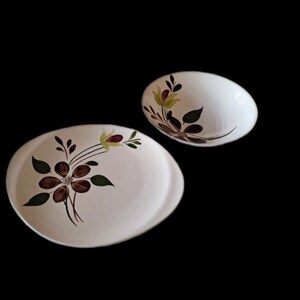 Pode incluir: Um prato oval branco para servir e uma tigela branca com um desenho floral em tons de marrom, verde e amarelo.