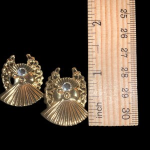 May include: Two gold angel-shaped ornaments with a clear rhinestone in the center of each. The ornaments are approximately 1 inch in diameter.