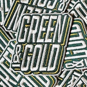 May include: Close-up of multiple green and gold embroidered patches that say "GREEN & GOLD" in white lettering.