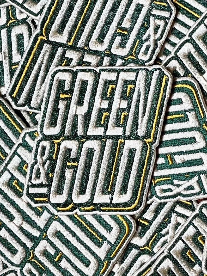 Może przedstawiać: Zbliżenie na kilka zielonych i złotych naszywek haftowanych z napisem "GREEN & GOLD" białymi literami.