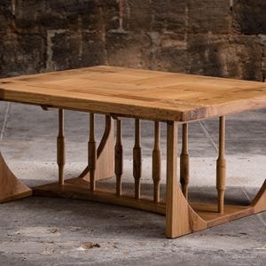 Peut inclure: Une table basse en bois avec une finition en bois naturel. La table a un plateau rectangulaire et un piétement unique en forme de cadre ouvert avec des lattes verticales.