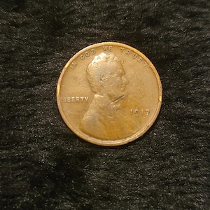 May include: A copper-colored 1917 Lincoln cent coin. The coin features the profile of Abraham Lincoln, the word "LIBERTY", and the inscription "IN GOD WE TRUST". The year "1917" is also visible.
