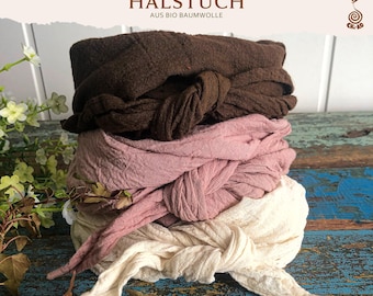 Könnte beinhalten: Ein Stapel aus drei geknoteten Stoffstirnbändern in Dunkelbraun, Altrosa und Creme. Jedes Stirnband besteht aus einem strukturierten, geknitterten Material mit einem mittigen Knoten. Der Text HALSTUCH AUS BIO BAUMWOLLE und ein Spirallogo sind sichtbar.
