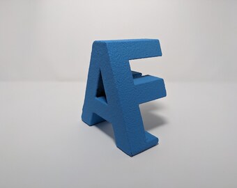 Pode incluir: Uma letra A e uma letra F impressas em 3D na cor azul, uma em cima da outra.