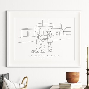 May include: A framed line art print depicting a marriage proposal scene in Discovery Park, Seattle, WA. The black and white illustration shows a person kneeling and offering a ring to another person. The print is displayed on a white wall.