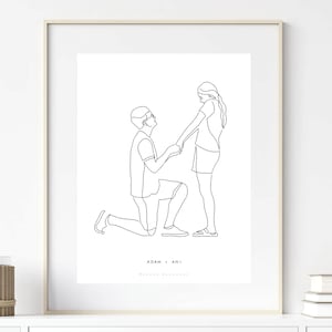 May include: Framed minimalist line art print depicting a marriage proposal. A man kneels before a woman, holding her hands. The artwork is in black and white, with the names "ADAM + ANI" at the bottom. The print is displayed in a white frame.