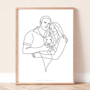 May include: A framed line art print featuring a couple embracing a small dog. The black line drawing style depicts the figures in a minimalist, modern aesthetic. The artwork is set against a white background, framed in a light wood.