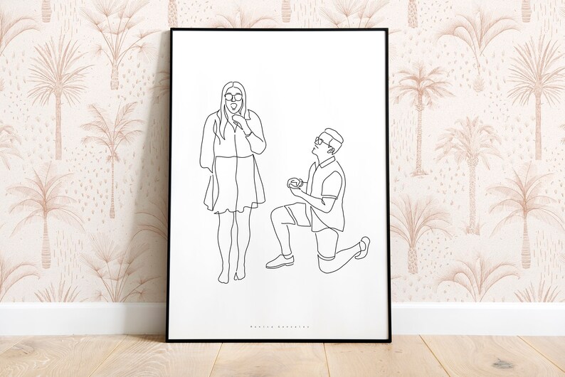 May include: Black framed line art print depicting a marriage proposal. A person kneels, presenting a ring to another person. The background features a beige wallpaper with a palm tree pattern.
