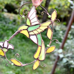 Pu&ograve; includere: Un colibr&igrave; in vetro colorato con pezzi di vetro giallo, verde e bianco, appollaiato su un ramo di filo con perline di vetro verdi. Il colibr&igrave; &egrave; in volo con le ali spiegate.