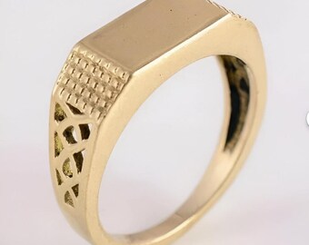 Könnte beinhalten: Goldener Siegelring mit rechteckiger Oberseite und aufwendigen Details an den Seiten. Der Ring hat eine polierte Oberfläche und ein klassisches Design, das für den Alltag geeignet ist. Der Ring hat ein glattes, abgerundetes Band.