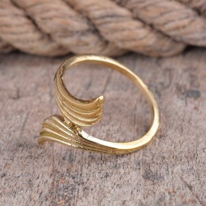 May include: A gold-colored ring with a swirling, open design. The ring features a textured, leaf-like detail on the band. The ring is set against a neutral background.