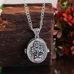 Peut inclure: Un collier avec un pendentif ovale argenté orné d'un motif floral. Le médaillon est suspendu à une chaîne délicate et présente un motif complexe de fleurs et de feuilles. Une petite pierre rose de forme ovale est sertie au bas du médaillon.