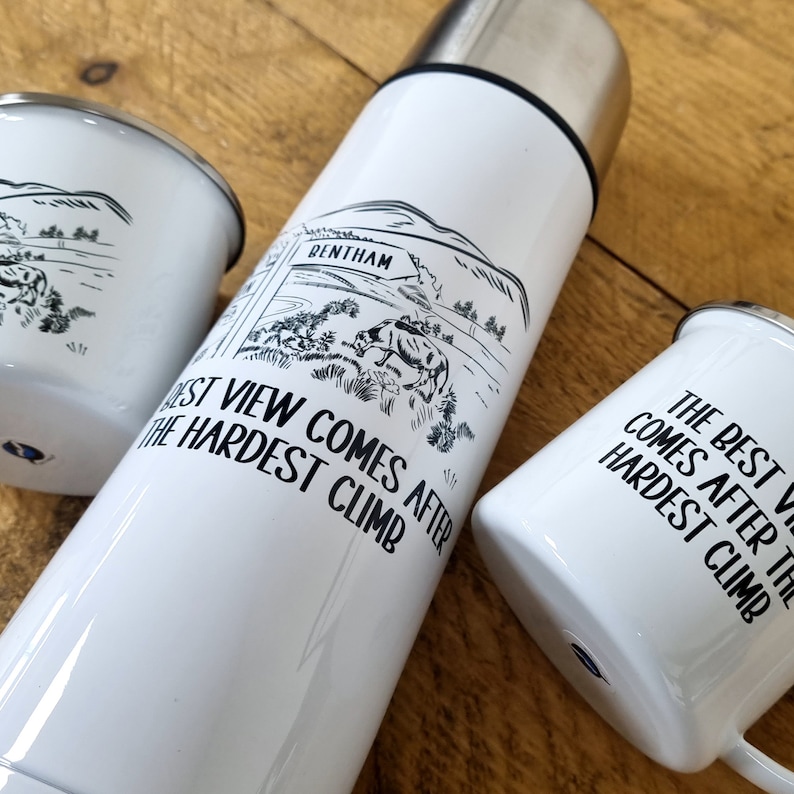 K&ouml;nnte beinhalten: Wei&szlig;e isolierte Reiseflasche mit einer Schwarzwei&szlig;illustration einer Kuh und einem Schild mit der Aufschrift "BENTHAM". Der Text "The best view comes after the hardest climb" ist auf die Flasche gedruckt.