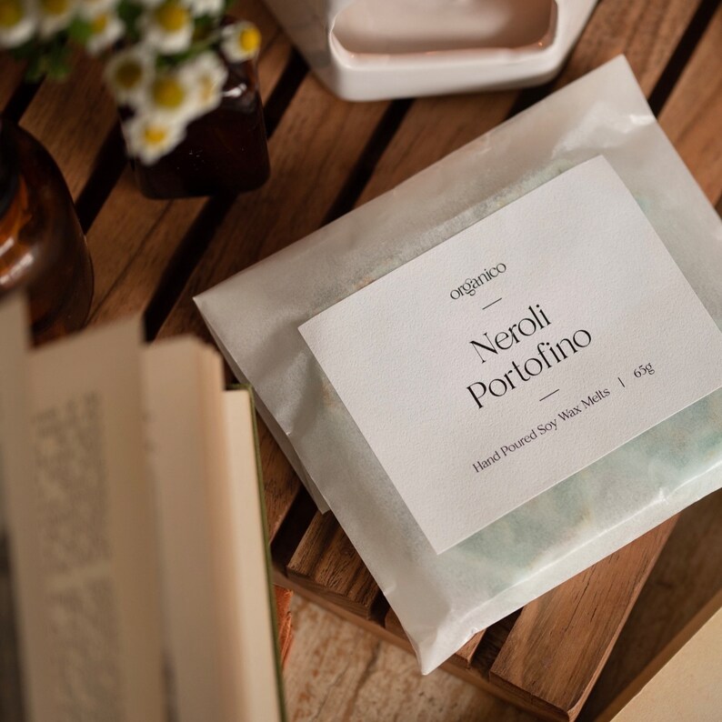 May include: A white paper bag with a label that reads "organico" and "Neroli Portofino" in black text. The label also says "Hand Poured Soy Wax Melts | 63g".