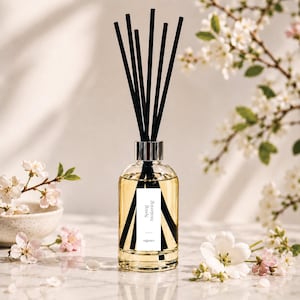 May include: A clear glass reed diffuser bottle filled with light yellow liquid, featuring a white rectangular label with the text "Spring Awakening" and "organico". Seven thin black reeds extend from the silver-toned neck of the bottle.