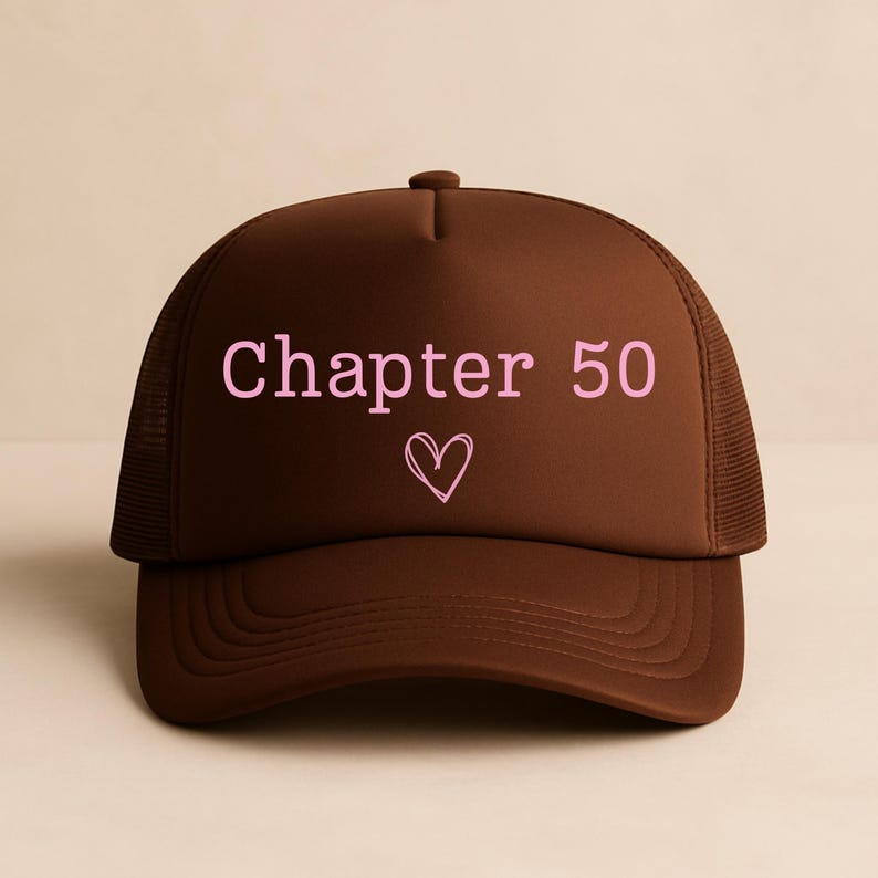 May include: A brown trucker hat with a curved brim and mesh back. The front of the hat features the text "Chapter 50" in pink, with a pink heart symbol below the text. The hat is designed for casual wear.