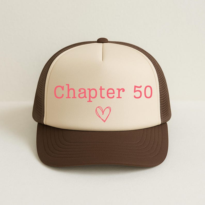 May include: A brown and tan trucker hat with the text "Chapter 50" in pink, along with a pink heart graphic. The hat has a mesh back and a curved brim.