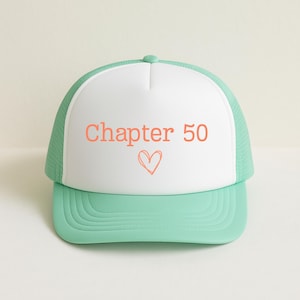 May include: A mint green and white trucker hat with the text "Chapter 50" in coral, along with a heart symbol. The hat has a curved brim and a mesh back.
