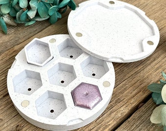 May include: White round container with a removable lid. The container has six hexagonal compartments and one round compartment. The lid is also white and has a speckled texture.