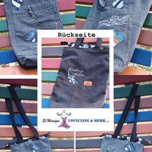 Könnte beinhalten: Eine graue Tragetasche aus Jeansstoff mit schwarzen Tragegriffen, Reißverschluss und mehreren Außentaschen. Die Tasche ist mit kleinen blauen Jeans-Herz-Applikationen verziert. Eine Seite zeigt den Sticktext "Handmade with Love" und einen Zweig.