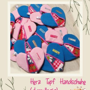 Può includere: Guanti da forno a forma di cuore in rosa e blu con accenti in tessuto floreale e a scacchi. I guanti sono etichettati con piccole etichette e il testo "Kochen & Backen mit Herz" è visualizzato sopra. È presente anche il testo "Cook Simply".