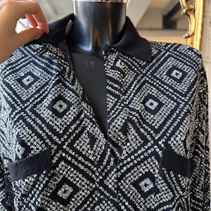 May include: A black and silver glittery collared shirt with a geometric pattern. The shirt has a v-neck and long sleeves.