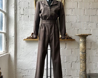 May include: A brown jumpsuit with a zipper closure and a collared neckline. The jumpsuit has a relaxed fit and is made of a soft, textured fabric.