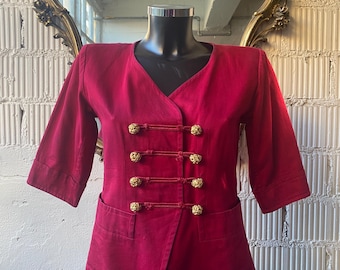 May include: A red cropped jacket with gold buttons and a V-neck. The jacket has a slightly fitted silhouette and is made of a smooth fabric.