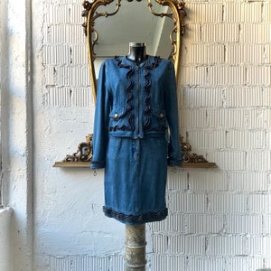 Peut inclure: Un ensemble veste et jupe en jean avec des volants noirs et des boutons dorés. La veste a une fermeture éclair. La jupe est mi-longue.