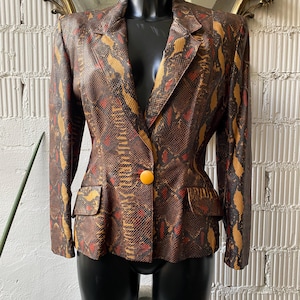 Può includere: Un blazer marrone, rosso e oro con motivo a stampa di pelle di serpente e un solo bottone giallo.