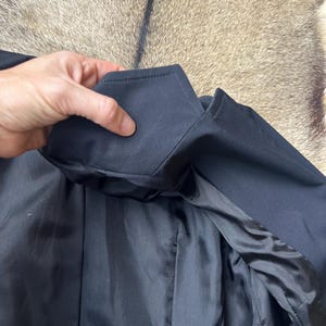 Pu&ograve; includere: Primo piano di un colletto e risvolto di giacca neri. La fodera interna &egrave; in tessuto nero lucido. La giacca &egrave; realizzata in un materiale scuro e liscio.