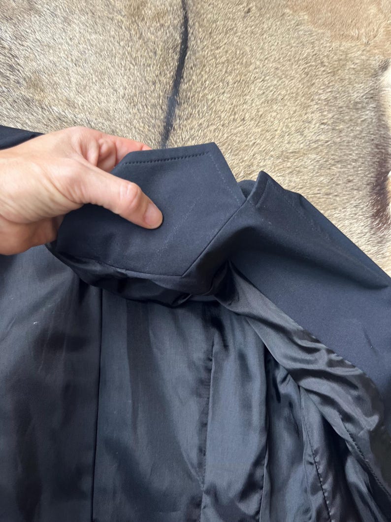 Pu&ograve; includere: Primo piano di un colletto e risvolto di giacca neri. La fodera interna &egrave; in tessuto nero lucido. La giacca &egrave; realizzata in un materiale scuro e liscio.