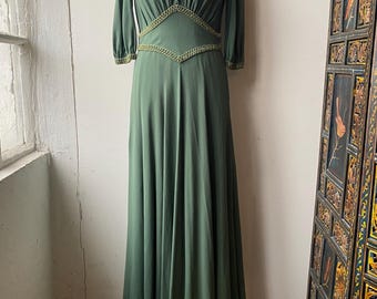 May include: A long, green maxi dress with a V-neckline and a gold trim around the neckline and waist.