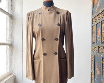 Op de afbeelding: Een bruine dubbelrijdige blazer met een mandarijnkraag en vier knopen. De blazer heeft twee zakken aan de voorkant en is gemaakt van een textuurstof.