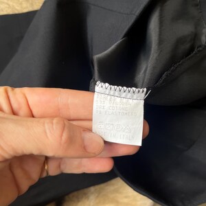 Pu&ograve; includere: Primo piano di un capo nero con un'etichetta bianca. L'etichetta presenta testo in italiano, inclusa la composizione del tessuto: 55% Viscosa, 36% Cotone e 9% Elastan. L'etichetta include anche simboli di cura e "MADE IN ITALY".