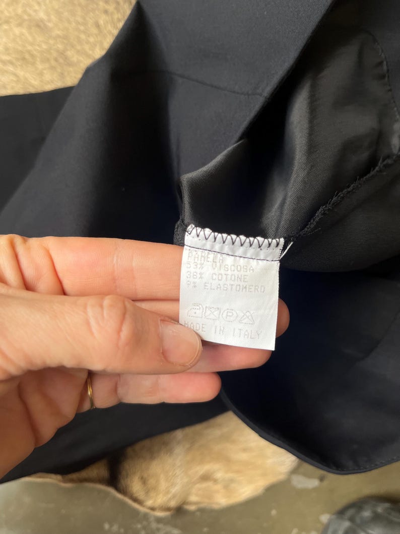Pu&ograve; includere: Primo piano di un capo nero con un'etichetta bianca. L'etichetta presenta testo in italiano, inclusa la composizione del tessuto: 55% Viscosa, 36% Cotone e 9% Elastan. L'etichetta include anche simboli di cura e "MADE IN ITALY".