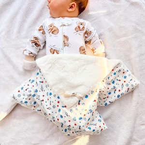 May include: A white long-sleeved baby sleeper featuring a brown koala print, paired with a white hooded blanket decorated with a colorful space-themed pattern of rockets, planets, and stars, featuring a soft, plush white faux fur lining.