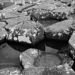Könnte beinhalten: Schwarz-Weiß-Bild einer natürlichen Felsformation, vermutlich Basaltsäulen. Die Felsen sind groß, unregelmäßig geformt und weisen teilweise Wasseransammlungen auf. Die Szene ist monochrom.