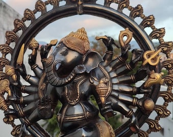 Könnte beinhalten: Eine schwarze und goldene Metallstatue von Ganesha, dem hinduistischen Gott der Anfänge, mit mehreren Armen, die verschiedene Gegenstände halten. Die Statue steht auf einem Sockel mit einem dekorativen Design.
