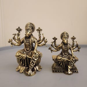 May include: Two metallic gold-toned statues of a multi-armed deity with a boar head, each adorned with intricate jewelry and headwear. The larger figure sits on a lotus-shaped base, while the smaller figure sits on a rectangular pedestal base.