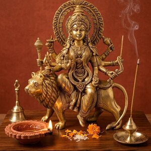 Può includere: Una statua in ottone di una divinità dalle braccia multiple a cavallo di un leone, con incisioni complesse e un'aureola circolare. La figura tiene in mano vari oggetti simbolici. Accanto alla statua ci sono una lampada a olio accesa e un incensiere.