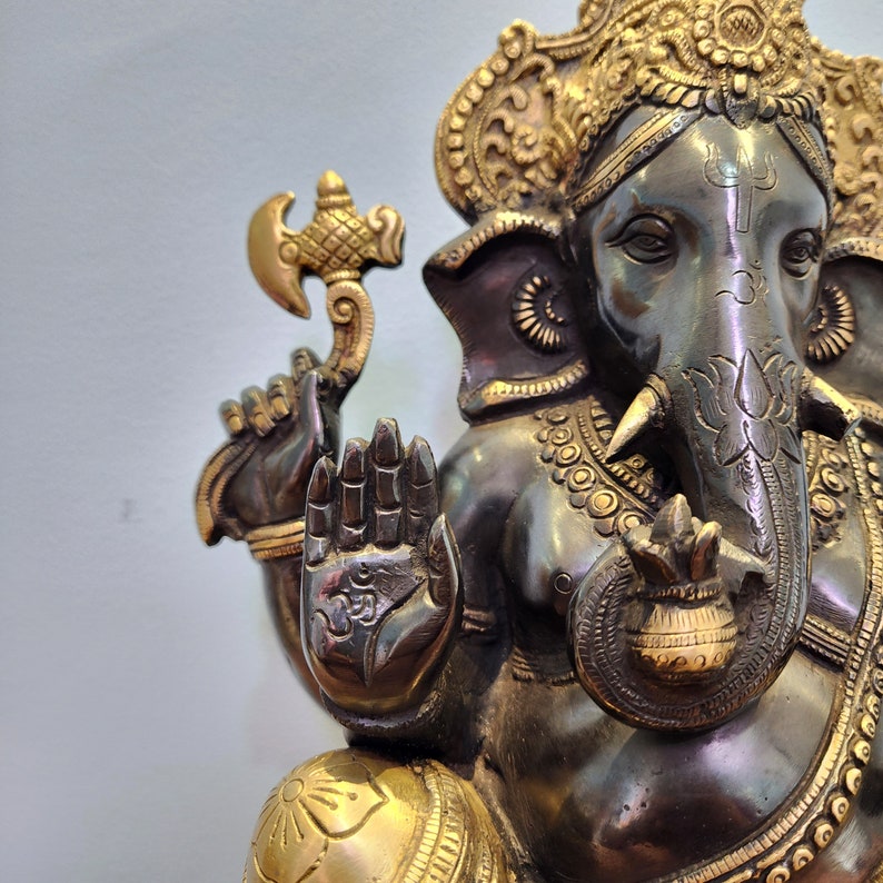 May include: A detailed bronze statue of Ganesha, the Hindu god of wisdom and prosperity. The statue features intricate details, including a golden crown, a trunk with a lotus flower, and a hand in a gesture of blessing.