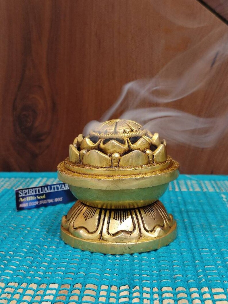 May include: A gold metal incense burner shaped like a lotus flower with a round base. Smoke is rising from the top of the burner.