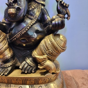 May include: A black and gold metal statue of Ganesha, the Hindu god of wisdom and prosperity. The statue is intricately detailed and features a rat at the base.